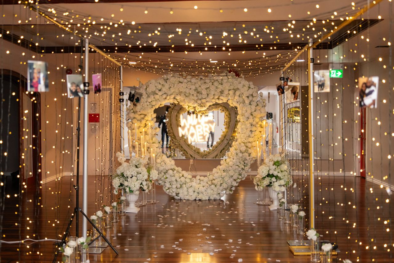 Fairy-light corridor leading to a white rose heart proposal arch